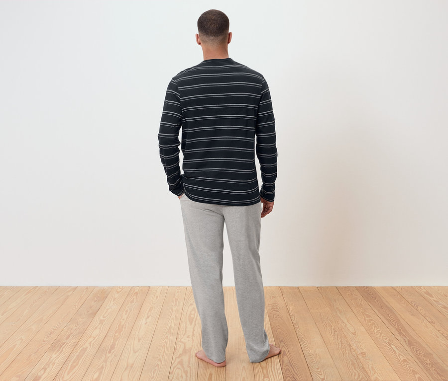 Ein Mann mit dem Rücken zur Kamera trägt ein gestreiftes Langarmshirt und eine graue Jogginghose.