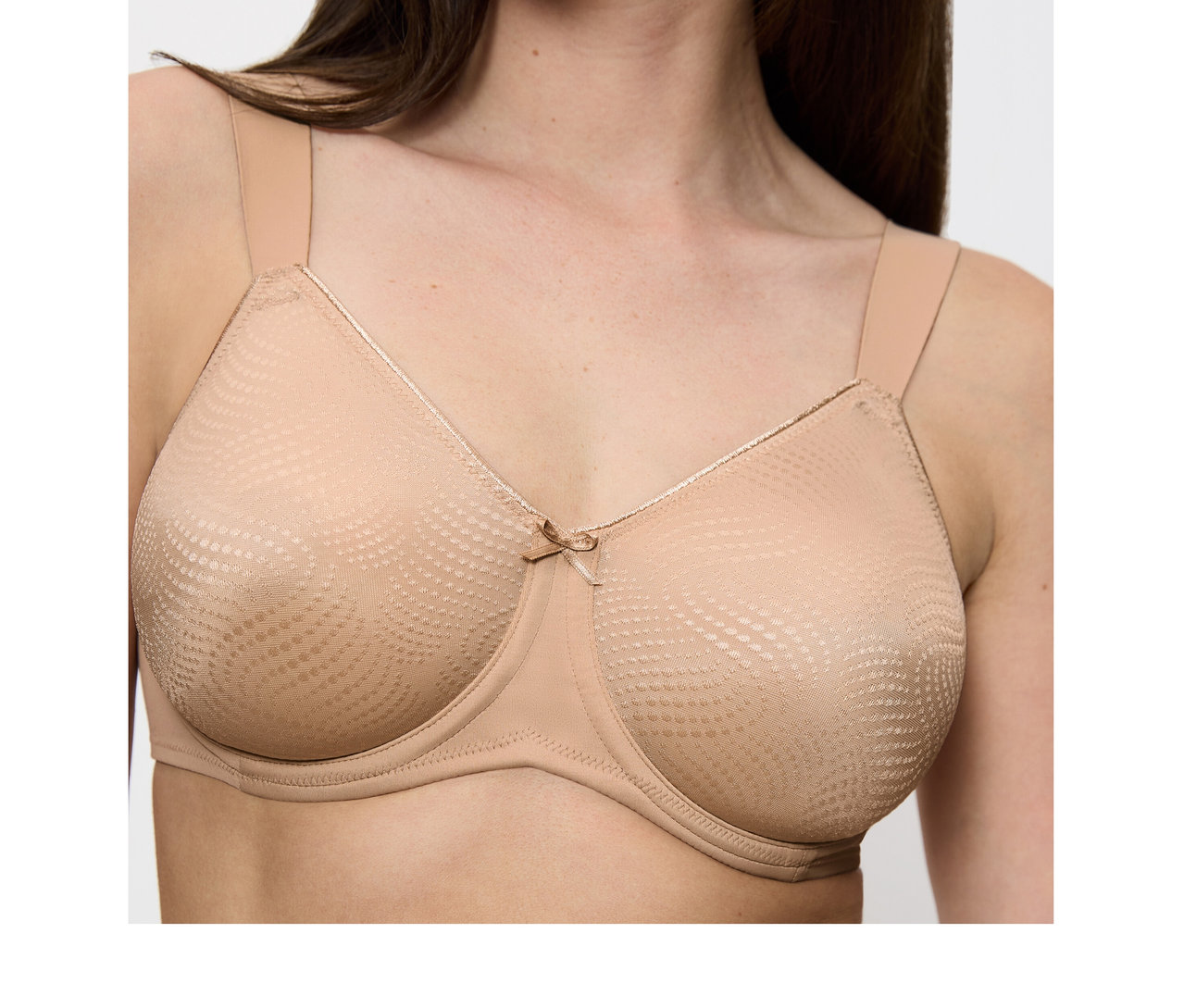 Frau trägt einen hautfarbenen Triumph Essential Minimizer W X BH mit breiten Trägern, strukturierten Cups und einer Schleife.