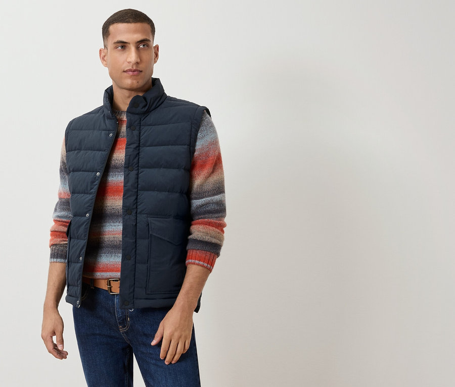 Mann trägt eine marineblaue Weste über einem gestreiften Pullover, einen braunen Gürtel und Jeans.