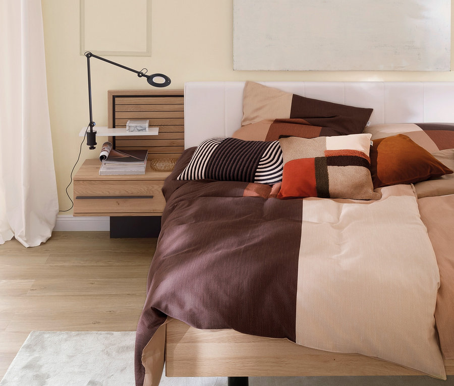 Bett mit braun-beiger Bettwäsche und Kissen.