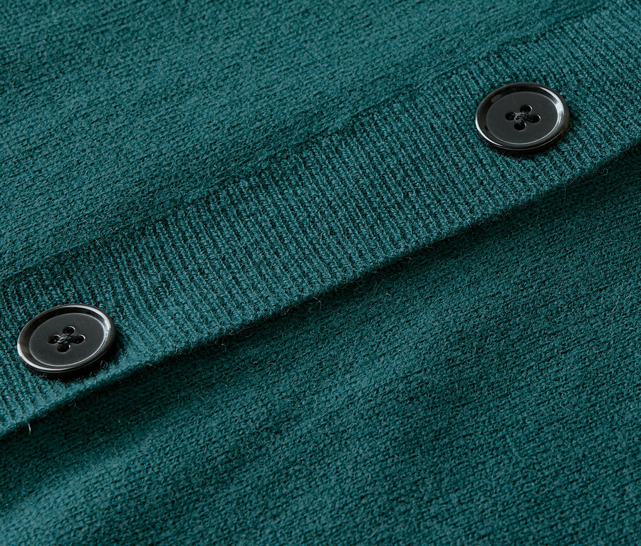 Detailaufnahme eines grünen Strickcardigans mit Knöpfen.