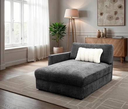 Graue Chaiselongue mit weißem Kissen auf beigem Teppich in einem Wohnzimmer.