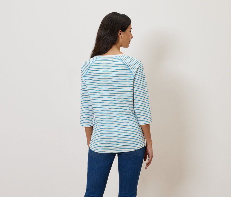 Rückansicht einer Frau mit langen, dunklen Haaren, die ein gestreiftes, dreiviertelärmeliges Oberteil und Jeans trägt.