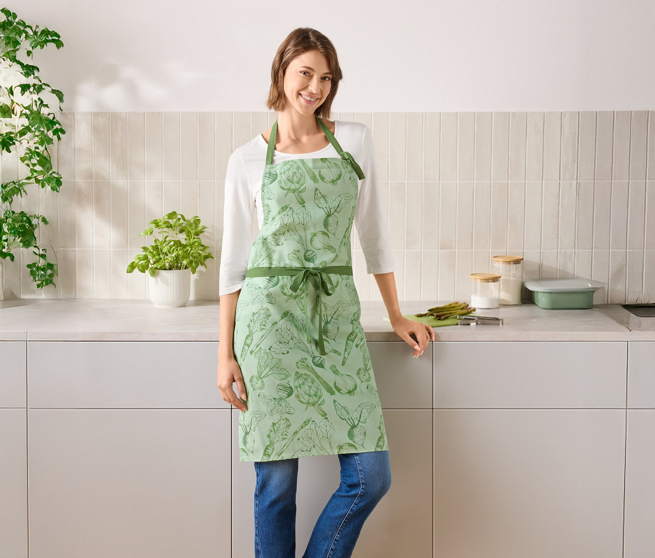 Eine Frau steht in einer Küche und trägt eine grüne Gemüseschürze.