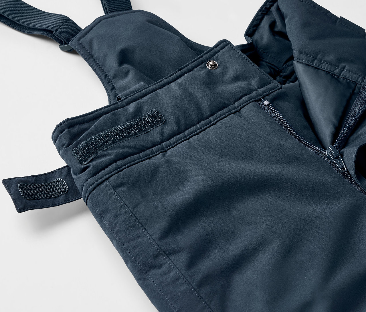 Detailaufnahme einer blauen Latzhose mit Reissverschluss und Klettverschluss.