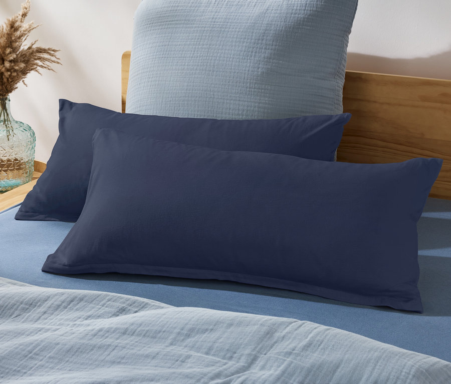 Zwei marineblaue Kissen auf einem blauen Bett mit hellblauer Decke und Vase mit Pampasgras.