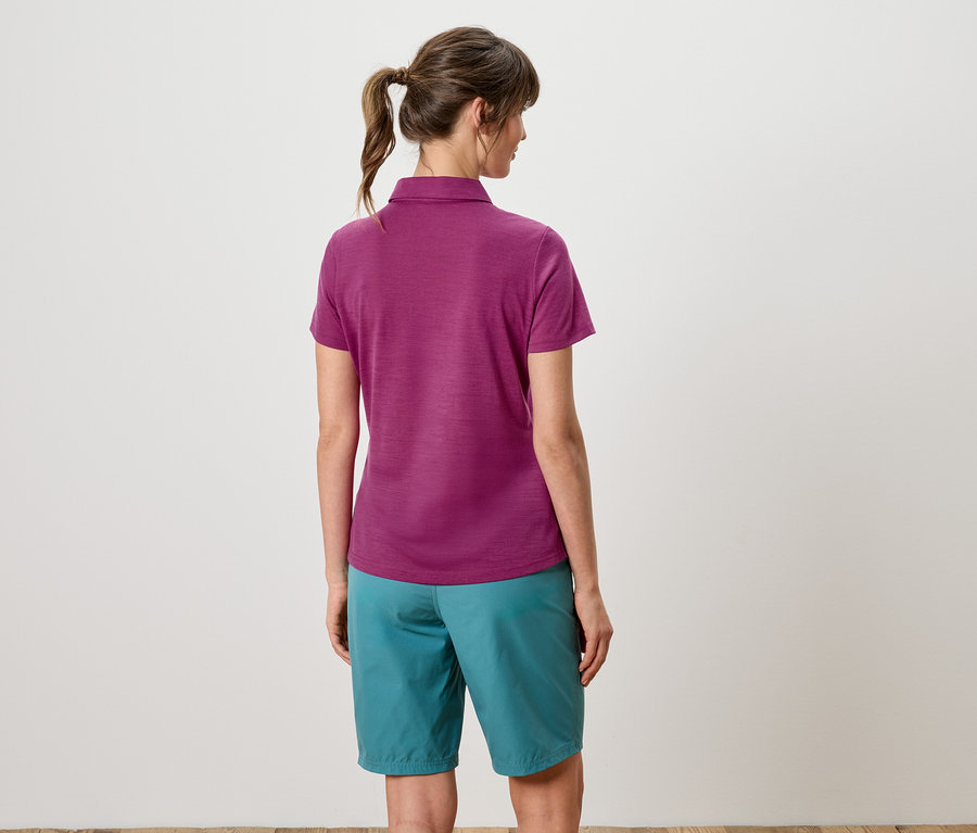 Rückansicht einer Frau mit Pferdeschwanz, die ein violettes Poloshirt und türkisfarbene Shorts trägt.