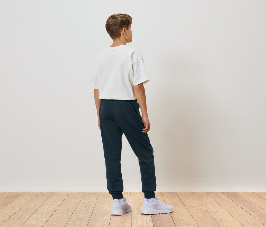Junge von hinten in einem weißen T-Shirt, blauen Jogginghose und weißen Turnschuhen.