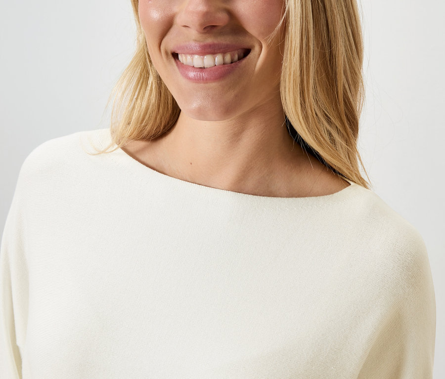 Frau lächelt und trägt einen cremefarbenen Pullover.