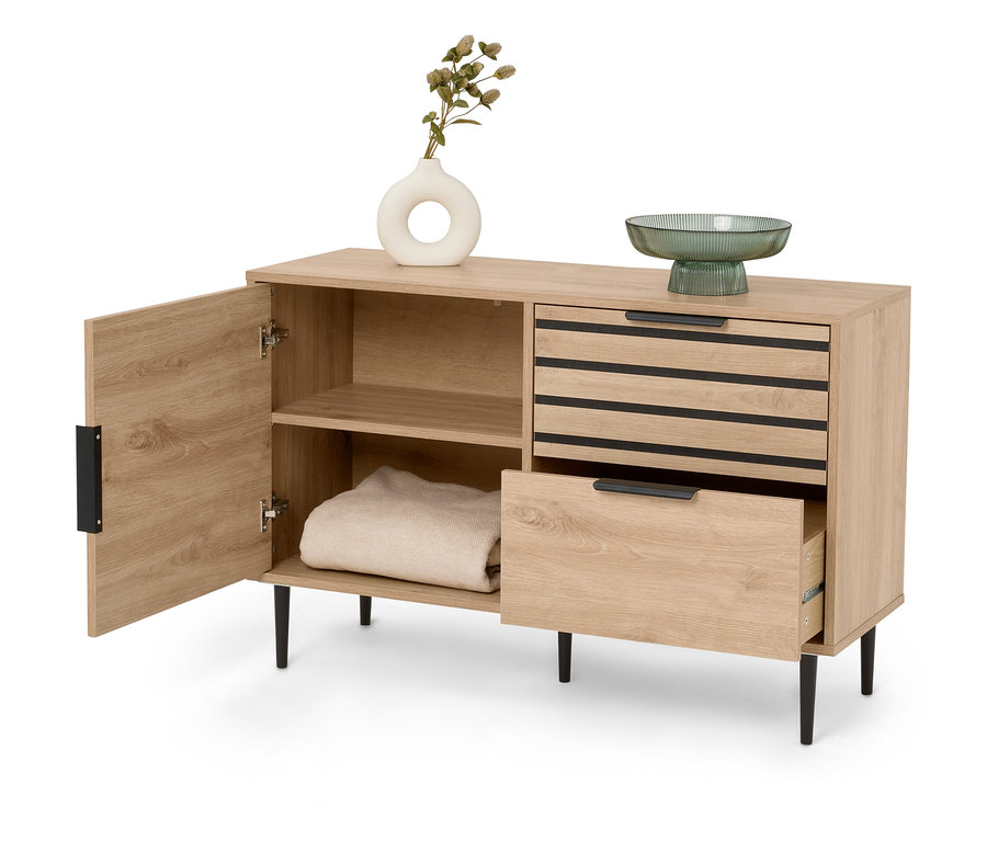 Ein Sideboard aus hellem Holz mit einer offenen Tür links, zwei Schubladen rechts und Deko-Elementen oben drauf.