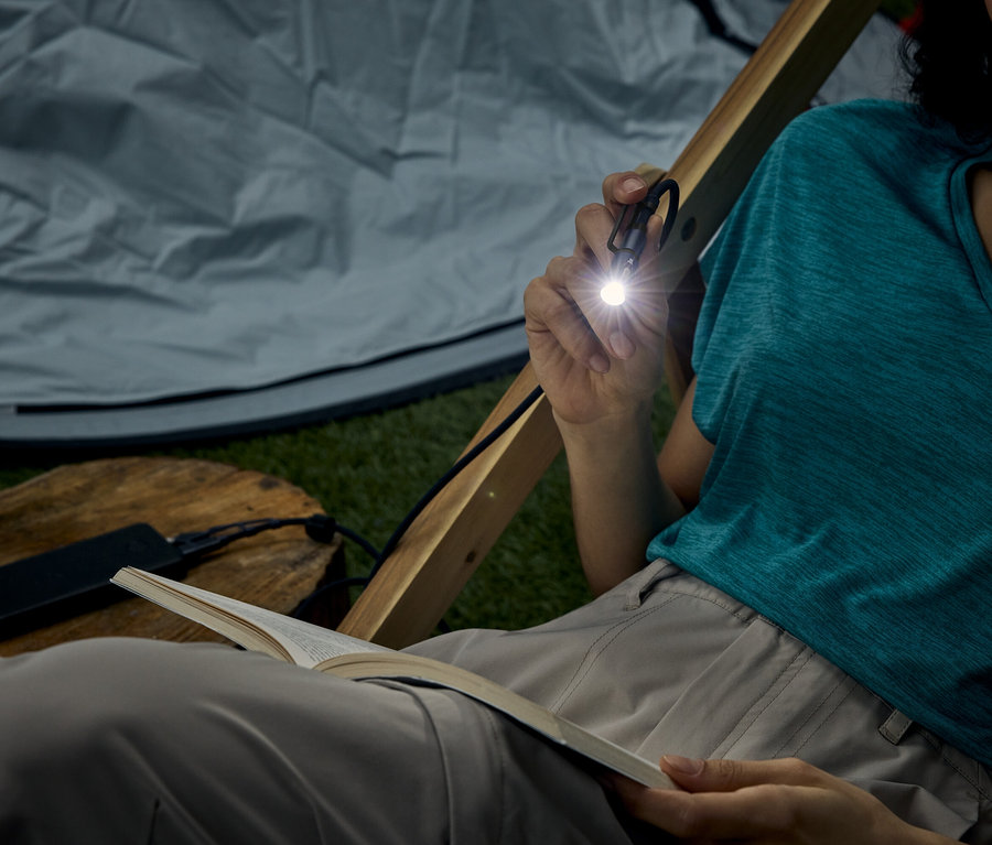 Frau sitzt im Zelt und liest ein Buch mit einer kleinen Taschenlampe, die sie hält.