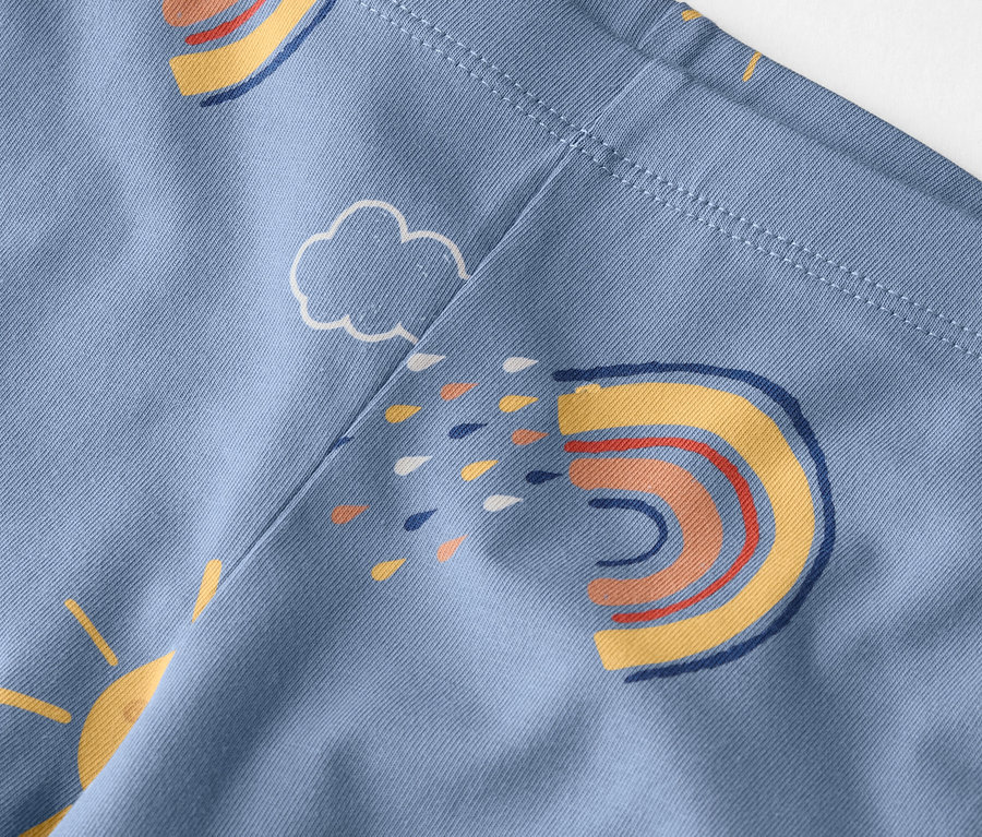 Nahaufnahme eines hellblauen Stoffes mit einem Muster aus Regenbögen, Sonnen und Wolken.