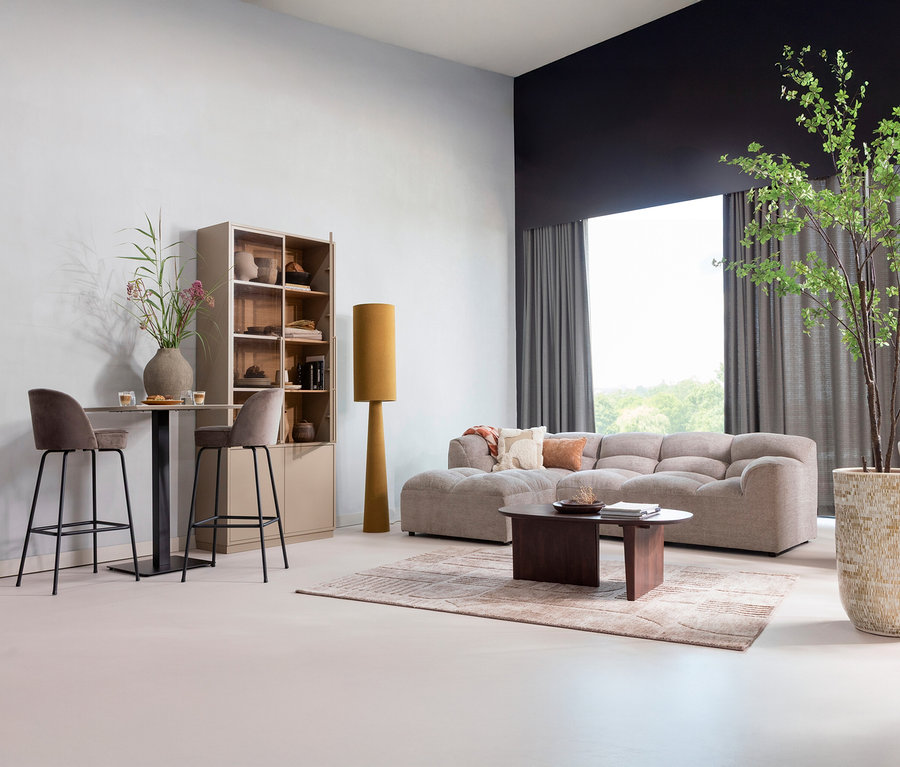 Wohnzimmer mit zwei Barhockern an einem Tisch, einem Bücherregal, einer Stehlampe, einem Sofa und einem Baum.