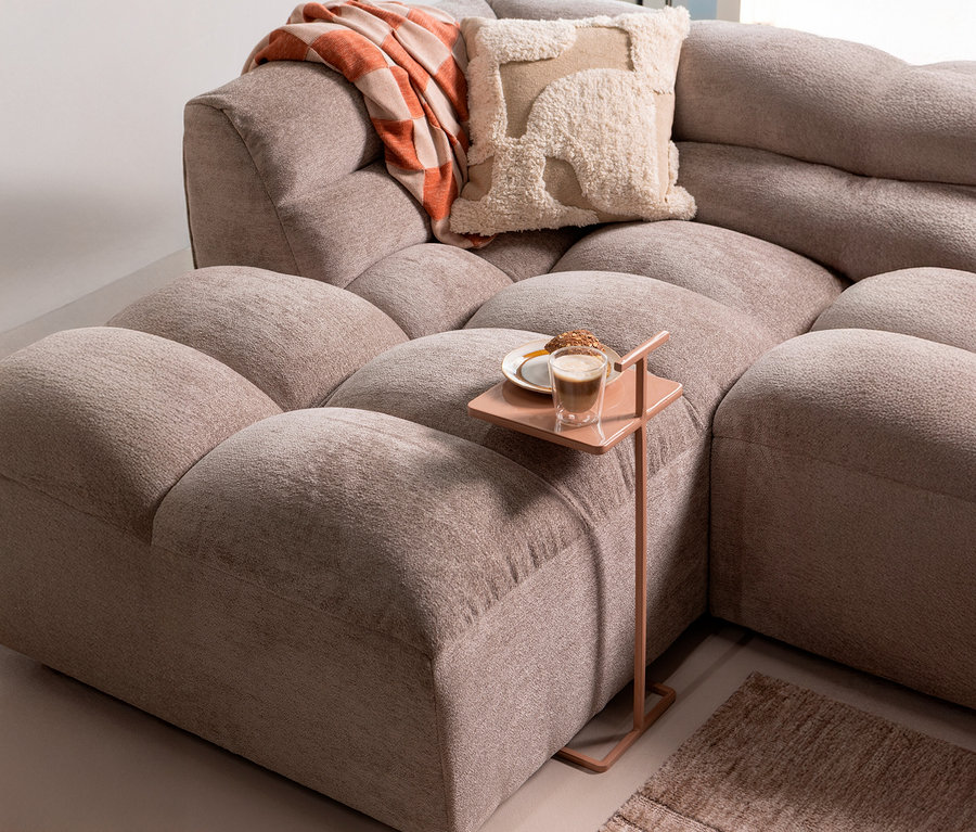 Detailaufnahme eines modularen Sofas mit einem Getränk und Gebäck auf einem Beistelltisch, darüber eine Decke und ein Kissen.