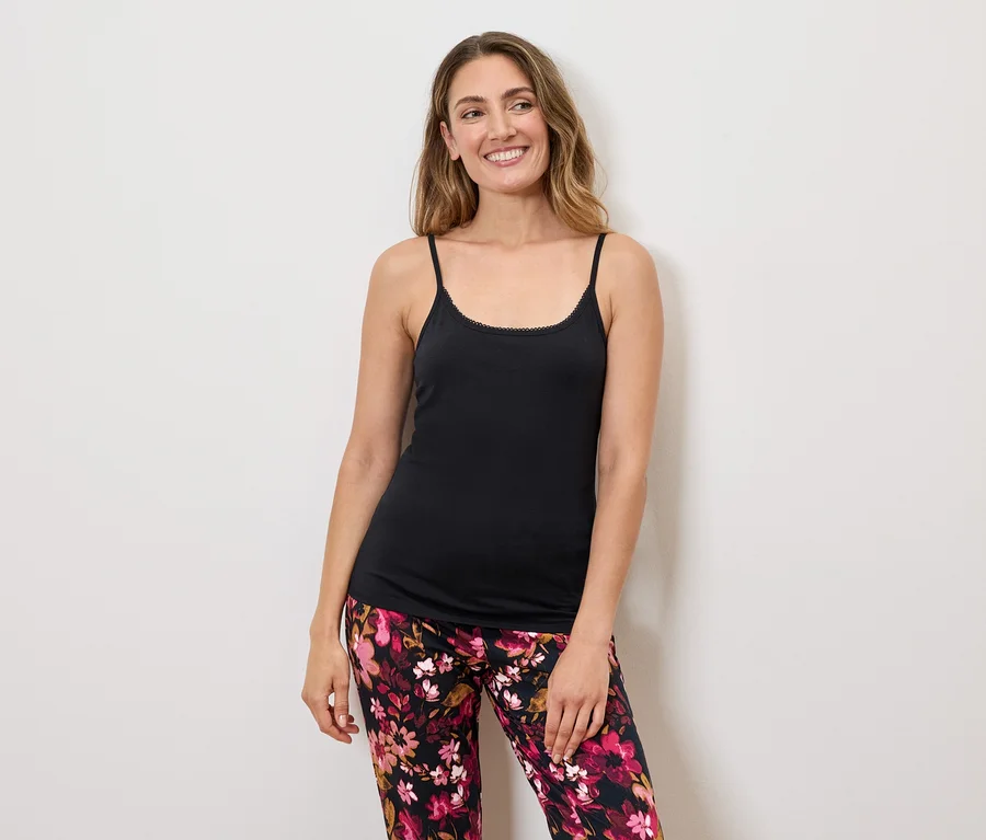 Frau mit langen Haaren, die ein schwarzes Tanktop mit Spaghettiträgern und eine blumengemusterte Hose trägt.