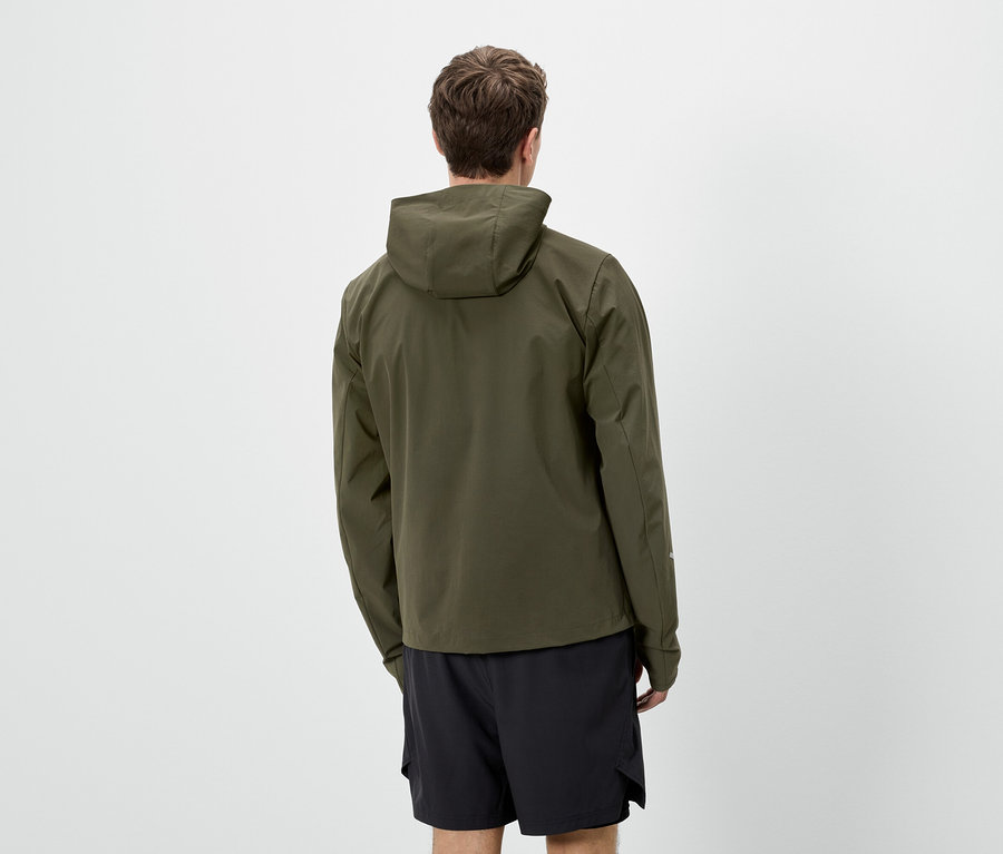 Mann von hinten in olivgrüner Jacke mit Kapuze und schwarzen Shorts vor weißem Hintergrund.