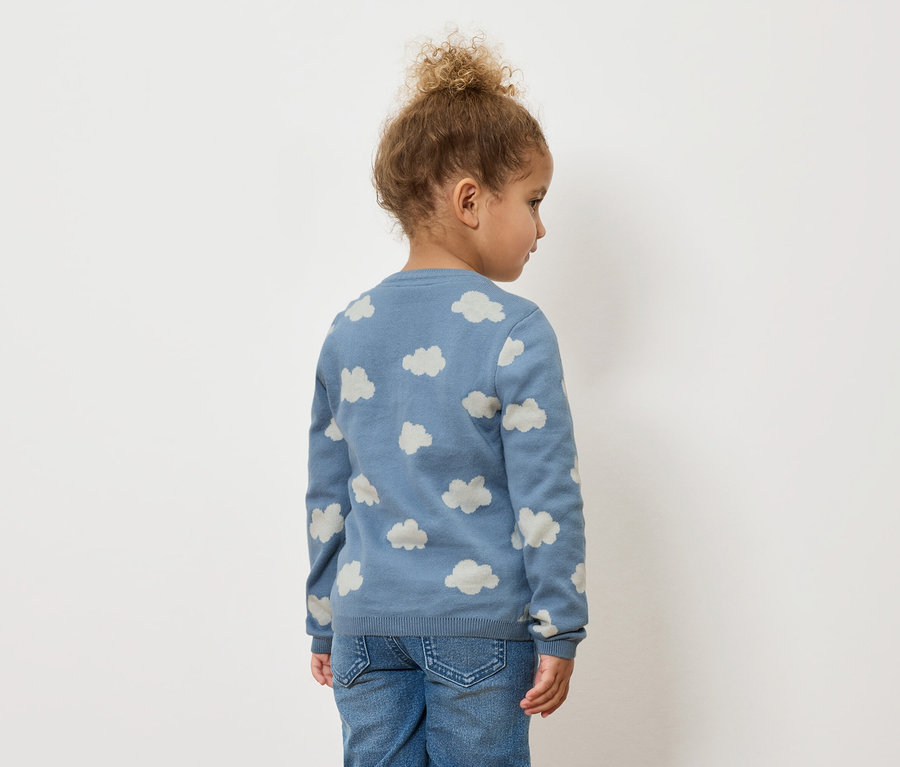 Kind von hinten, trägt einen blauen Pullover mit Wolkenmuster und Jeans.