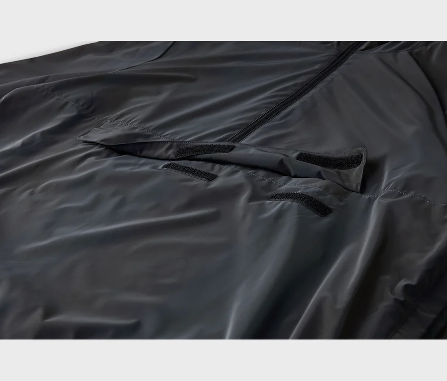 Dunkelgraue, leicht glänzende Jacke mit schwarzem Reißverschluss und einer vorderen Pattentasche mit drei schwarzen Klettverschlüssen.