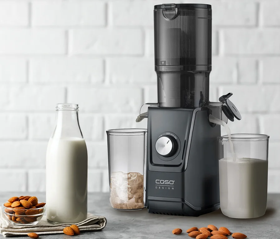 Schwarzer CASO Juice Fit Entsafter bereitet Mandelmilch zu, die in ein Glas fließt, daneben ein Glas mit Trester, eine Schale Mandeln und eine Milchflasche.