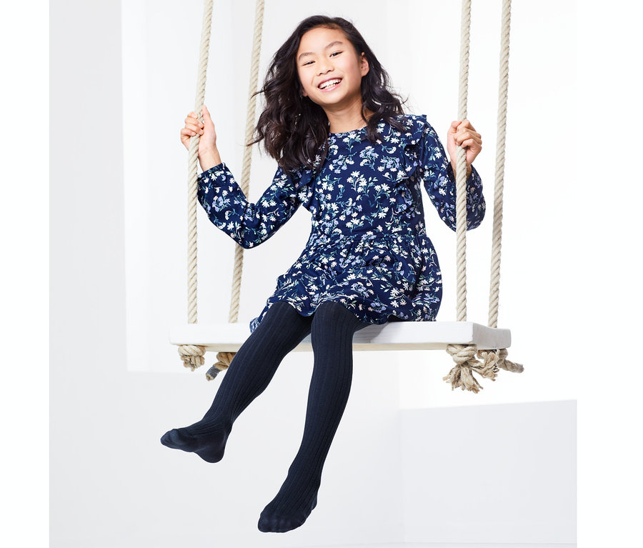 Asiatisches Mädchen mit blauem Blumenkleid sitzt auf einer Schaukel und trägt 2 Strumpfhosen.
