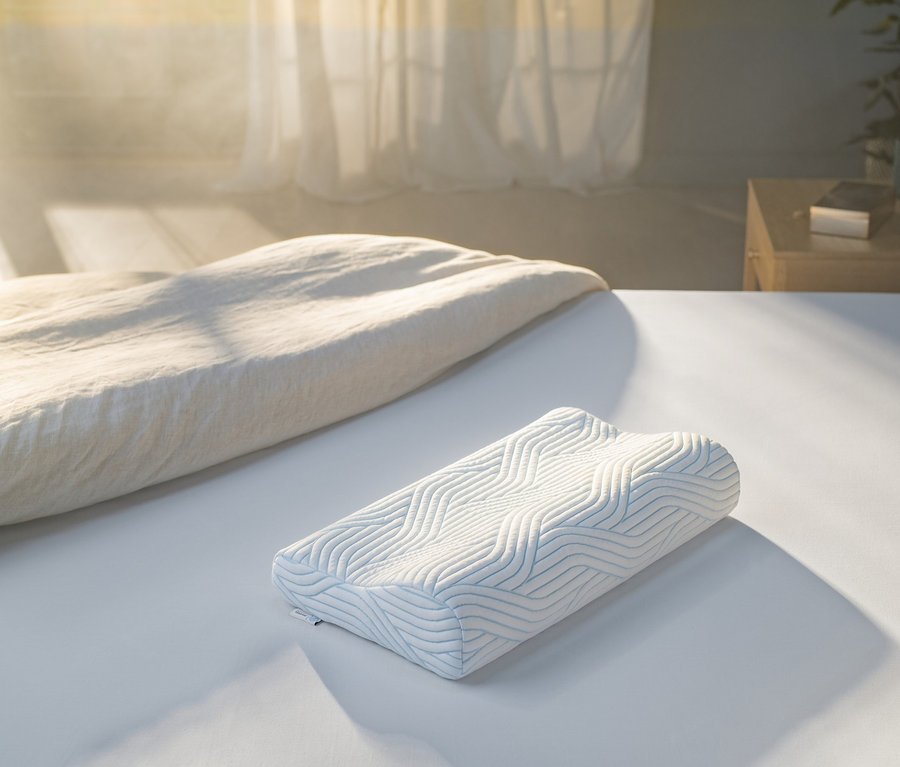 Auf einem weißen Bett liegt ein weißes TEMPUR® Shape Queen SmartCool™ Schlafkissen mit blauen Wellen.