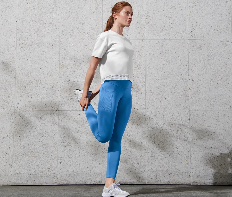 Frau dehnt Bein, trägt blaue Sporttight »pockets«.