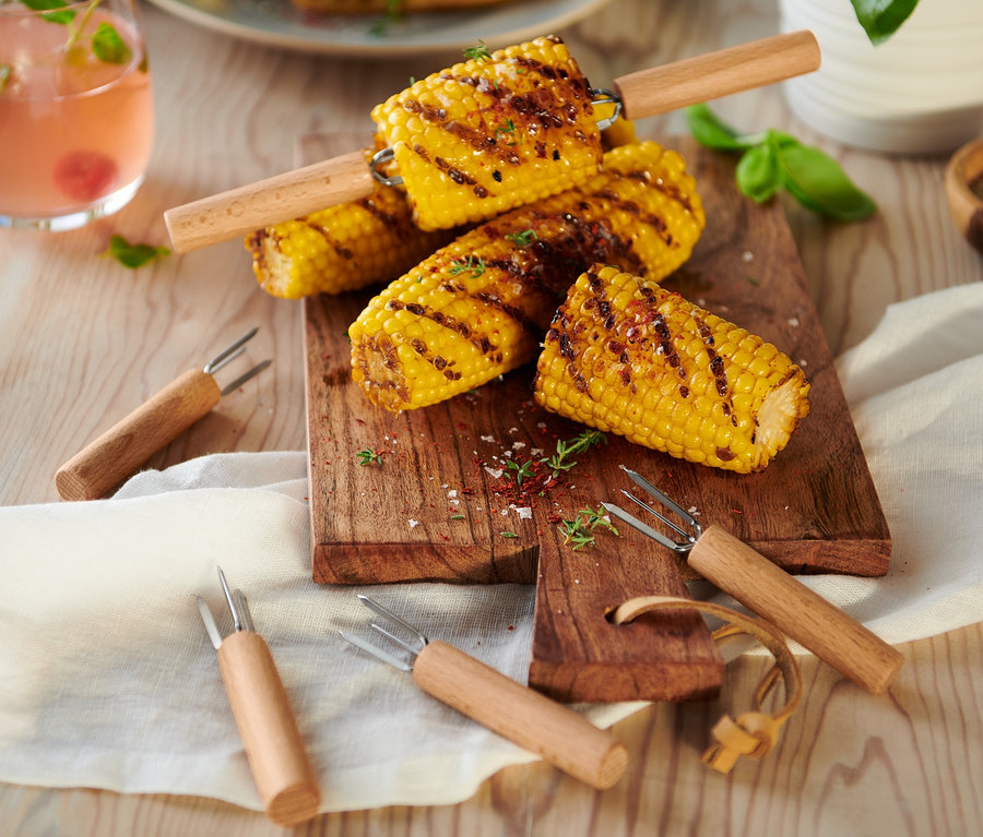 Gegrillter Mais auf einem Holzbrett mit 8 Maiskolbenhaltern.