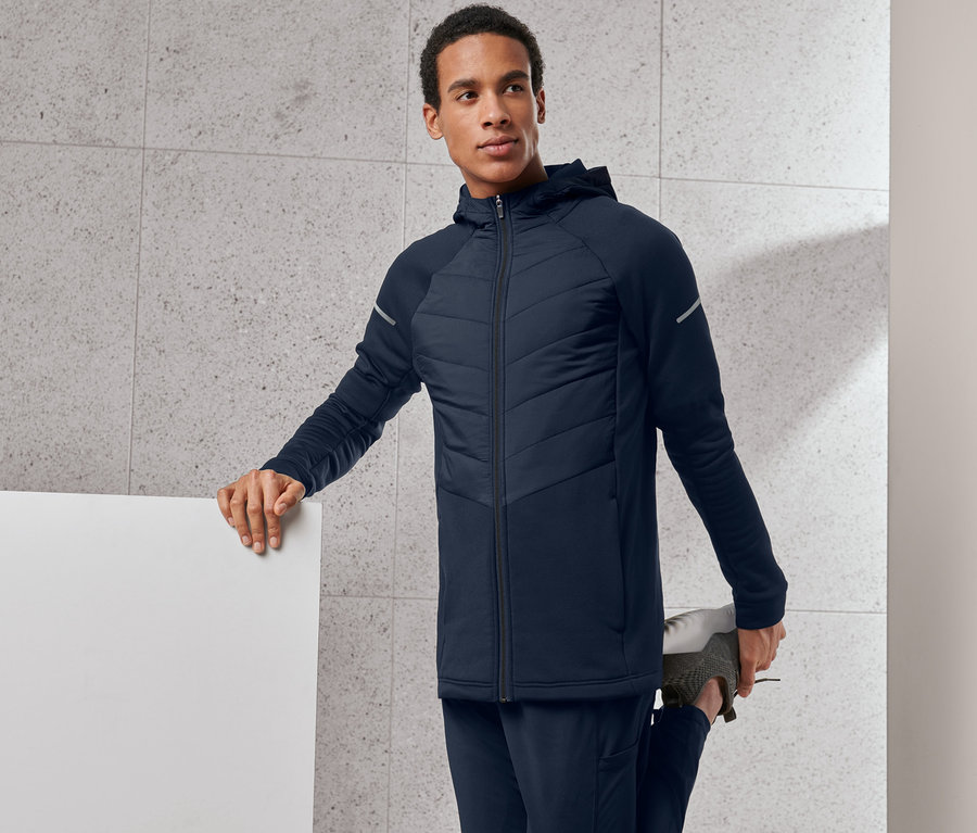 Mann dehnt sein Bein und trägt eine blaue Thermojacke.