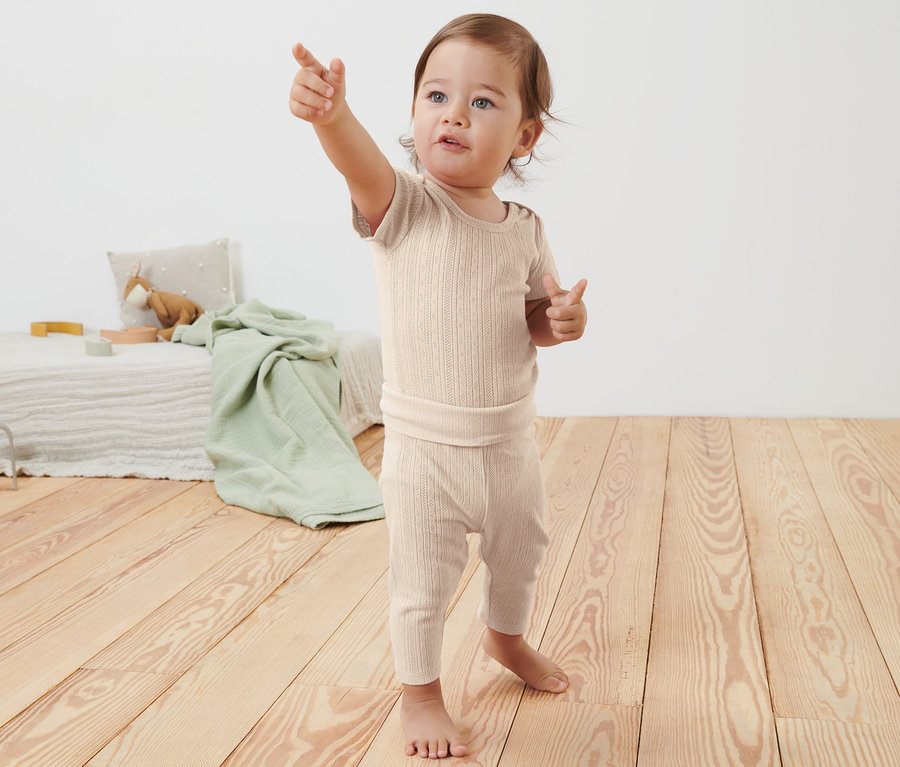 Baby in Body und Leggings zeigt mit dem Finger.