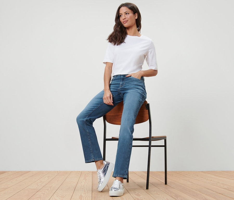 Frau sitzt auf einem Stuhl und trägt eine Straight Jeans – Fit »Kira« und ein weißes T-Shirt.