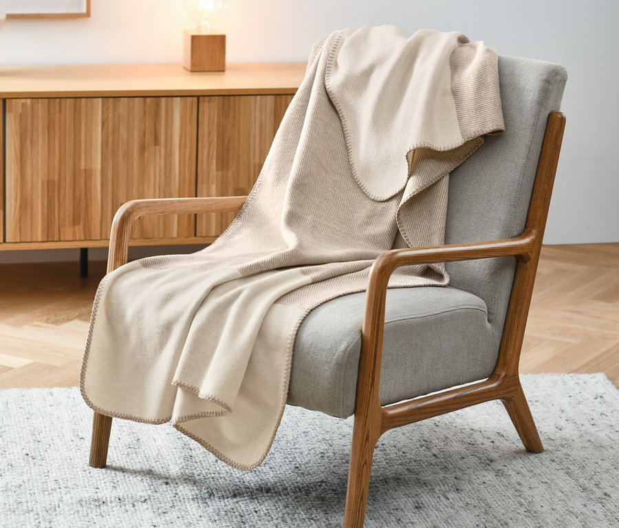 Beige Wohndecke über einem grauen Sessel.