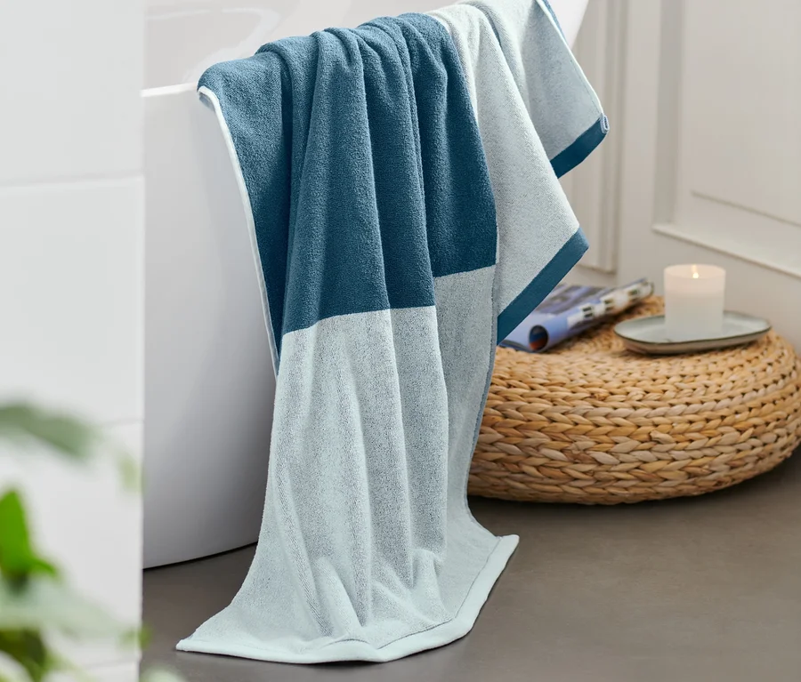 Blaues Jacquard-Badetuch liegt über dem Badewannenrand.