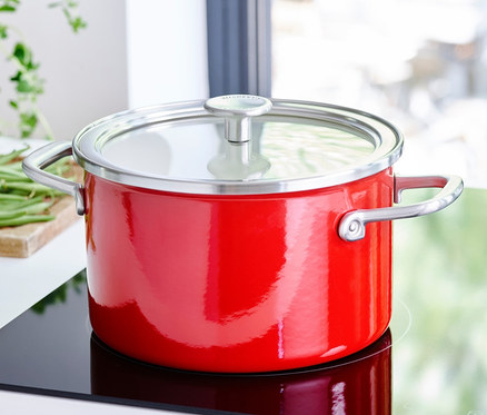 Roter KitchenAid Steel Core Emaille Kochtopf mit Deckel auf einem Kochfeld.