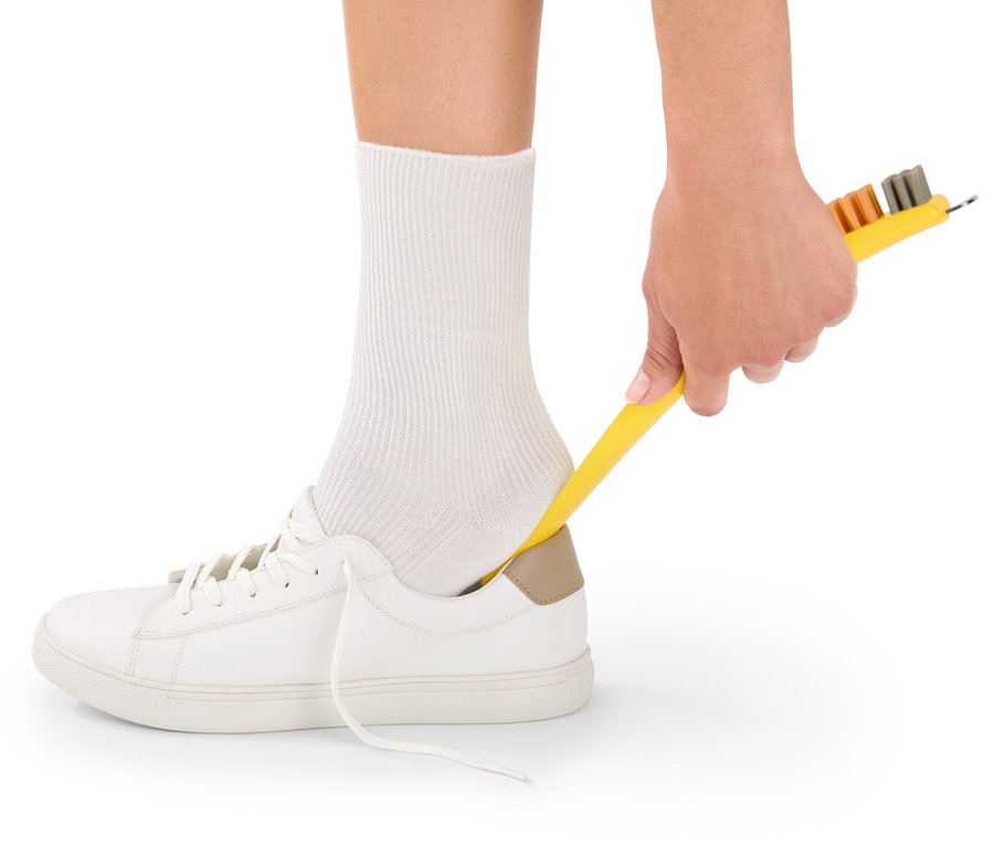 Eine Hand hält eine gelbe 3-in-1-Schuhreinigungsbürste und reinigt damit einen weißen Schuh.