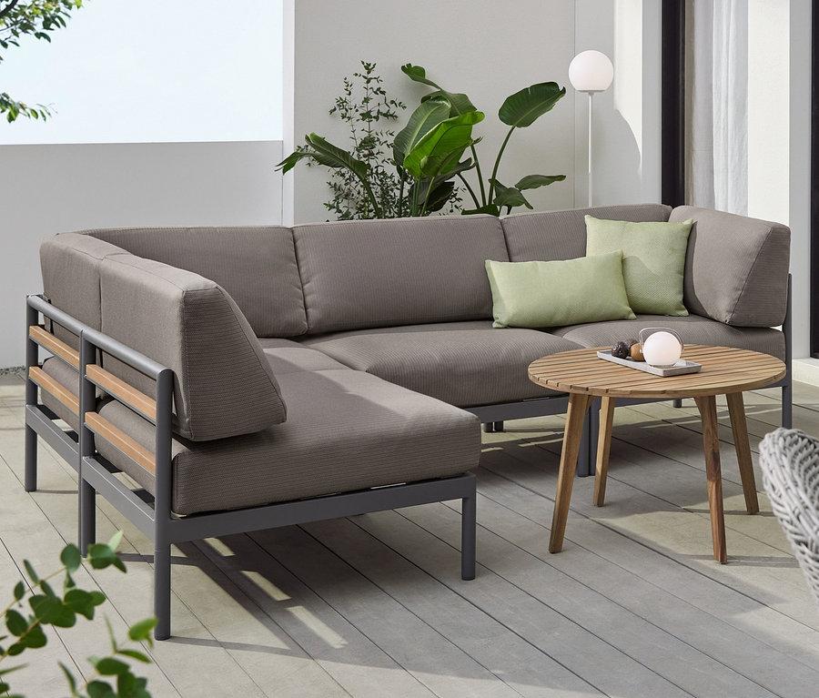 Eine graue Eckcouch mit Premium-Polsterbezügen, ein runder Couchtisch und ein Beistelltisch »Lenja« mit 2 Ebenen. Auf den Tischen stehen LED-Akkuleuchten.