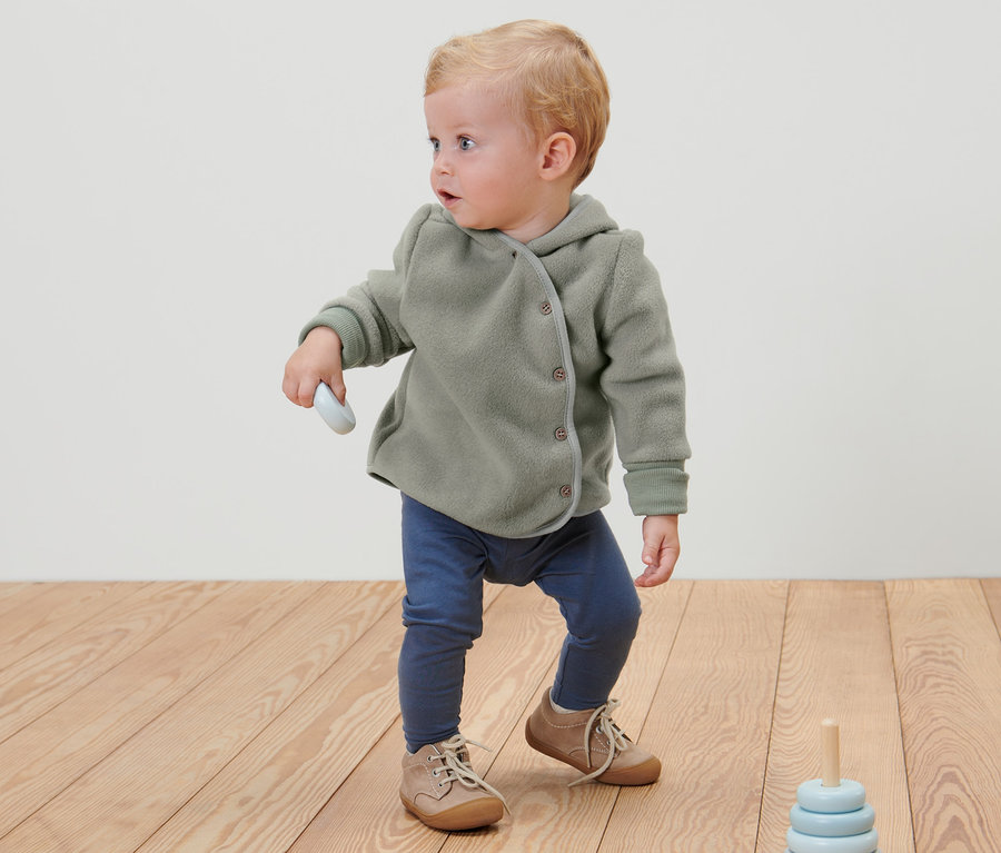Ein Kind steht auf einem Holzboden und trägt eine Baby- Kleinkind-Fleecejacke.