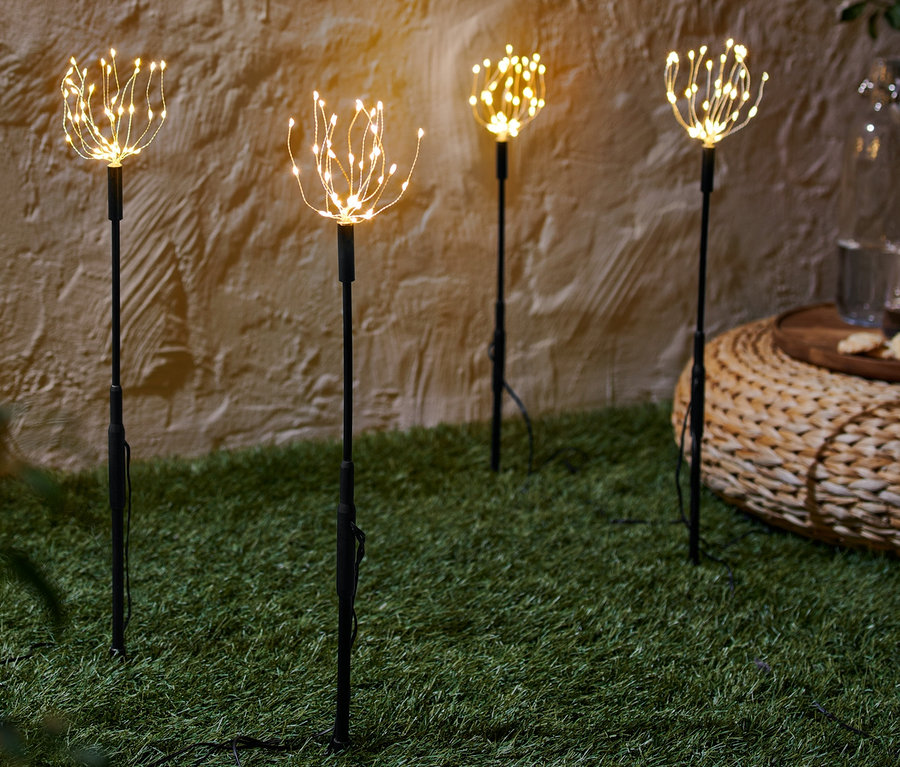 Vier LED-Gartenstecker stehen auf einer Wiese.