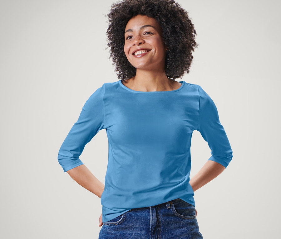 Frau posiert in hellblauem Shirt mit 3/4-Arm und blauen Jeans.