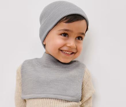 Ein lächelnder Junge trägt einen Kinder-Woll-Rollkragenschal und eine Mütze.