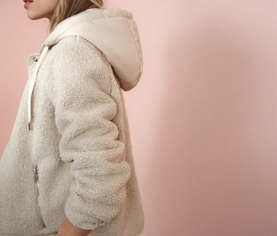 Frau trägt eine Street One Teddyjacke mit abnehmbarer Kapuze vor einem rosa Hintergrund.