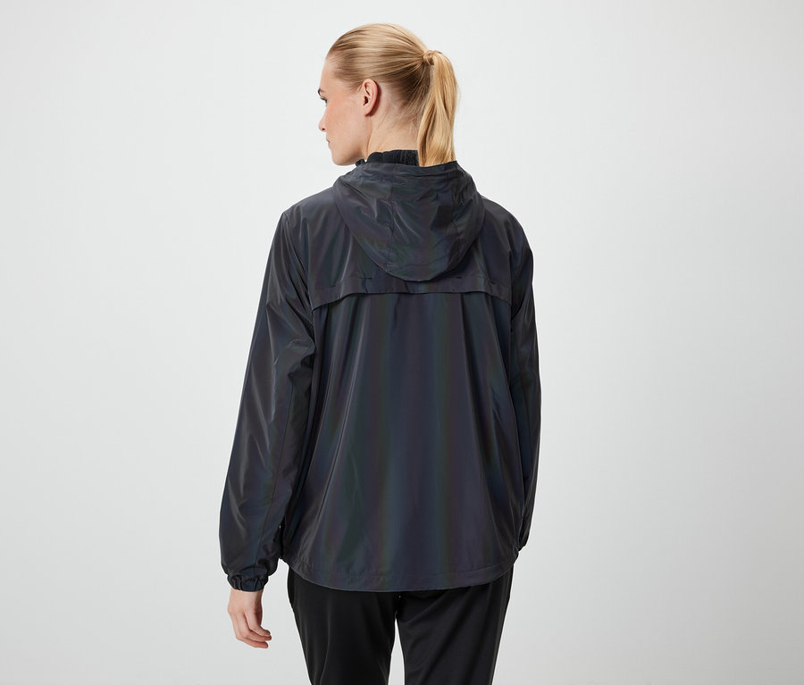 Rückansicht einer Frau mit blonden, zu einem Pferdeschwanz zusammengebundenen Haaren, die eine dunkle Kapuzenjacke und eine schwarze Hose trägt.