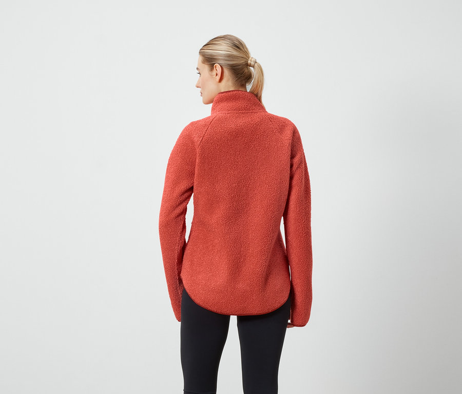 Frau mit dem Rücken zur Kamera trägt einen orangefarbenen Fleecepullover und schwarze Leggings.