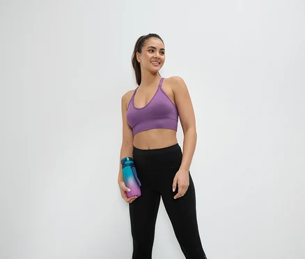 Frau im Sport-BH und Leggings hält eine Wasserflasche.