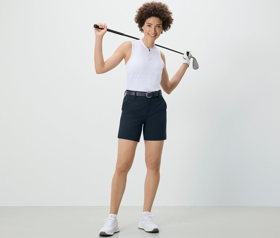 Frau hält Golfschläger über den Schultern und trägt dunkelblaue Softshell-Funktionsshorts.