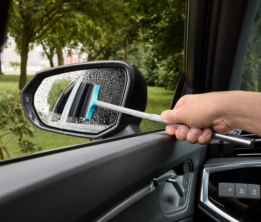Mann wischt mit einem Abzieher mit blauem Gummi Wasser von einem Auto-Seitenspiegel.