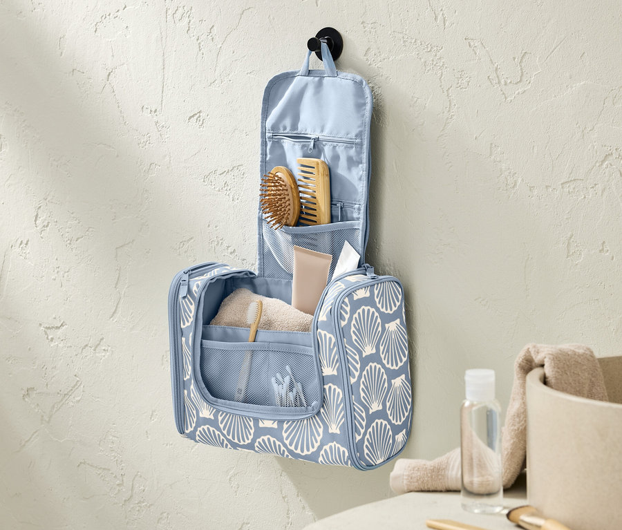 Eine blaue Kulturtasche mit Muschelmuster hängt an einer Badezimmerwand.