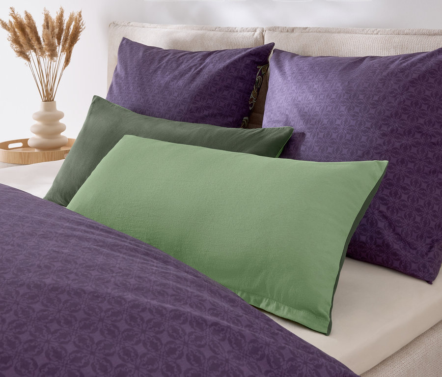 Lila- und grüne Kissen und eine Bettdecke liegen auf einem Bett.