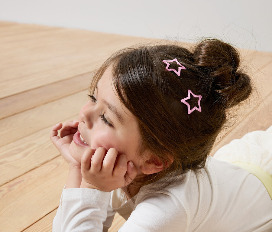 Mädchen liegt auf dem Boden mit rosafarbenen Stern-Haarspangen im Haar.