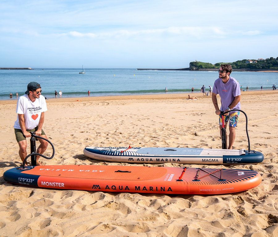 Zwei Männer pumpen Aqua Marina SUP Boards am Strand auf.