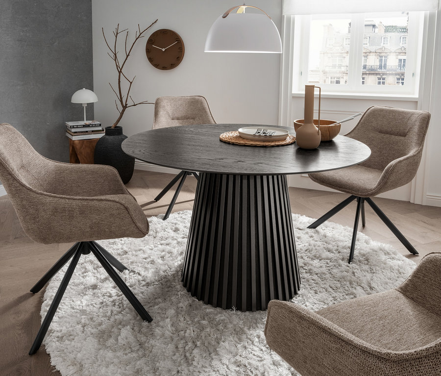 Vier hellbraune deVries San Carlo Essessel um einen runden deVries Andria Black Oak Esstisch auf einem weißen Teppich.